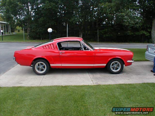 Red 1965 Ford Mustang fastback with white racing stripes and chrome trim