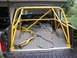 1988 Ford Bronco - Rear view of a black pickup truck with a yellow roll cage installed in the bed and a cracked windshield.