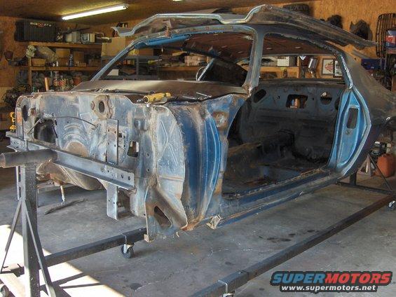Car body on stands, missing engine and most body panels. Looks like a 1970s muscle car