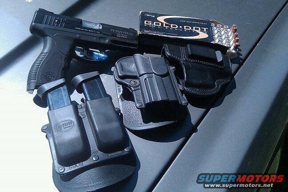 pistol with two magazines, a box of Gold Dot ammunition, and two holsters on a car hood
