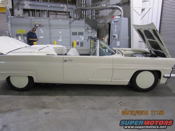 White convertible with hood open, side view, in an industrial setting