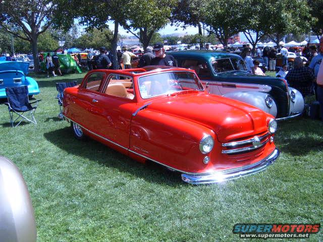 Red vintage car with chrome grille and round headlights parked on grass