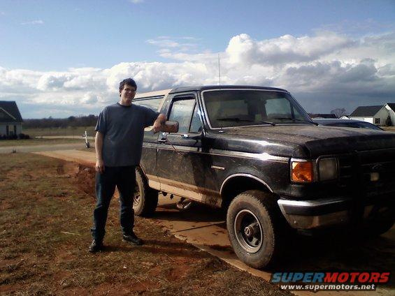 Black 1990 Ford Bronco parked on a concrete pad with a man beside it