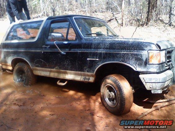 1990 Ford Bronco stuck in mud with someone pushing on the roof
