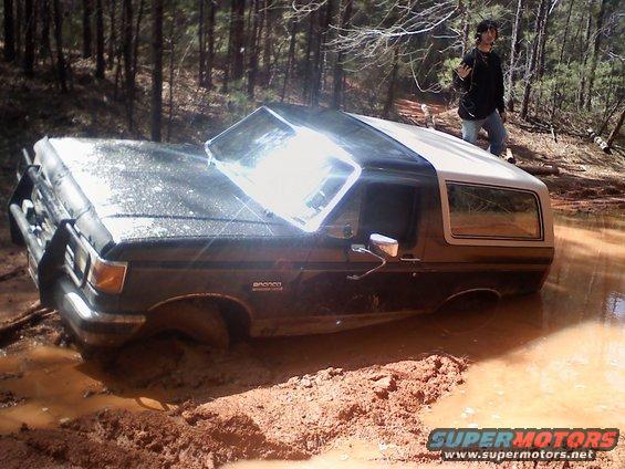 Ford Bronco stuck deep in mud with a person standing nearby