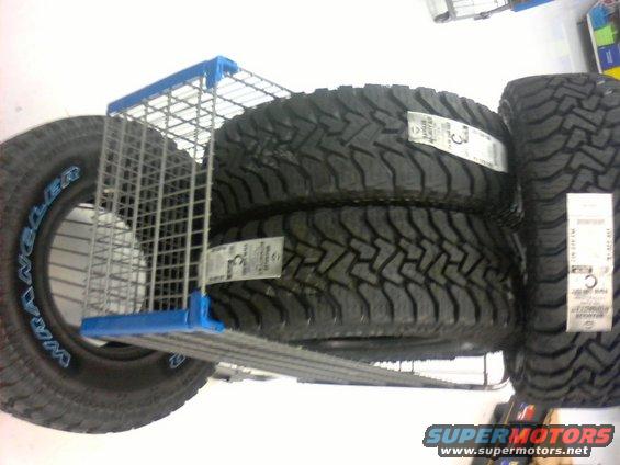 Stack of Goodyear Wrangler off-road tires on a store shelf with a shopping cart divider