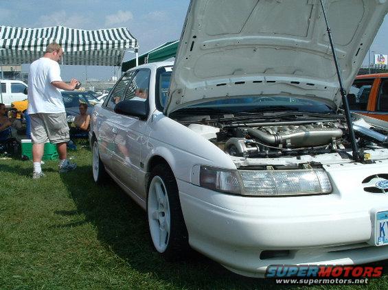 White 1993 Ford Taurus with hood open showing engine and turbocharger. White wheels and aftermarket exhaust visible