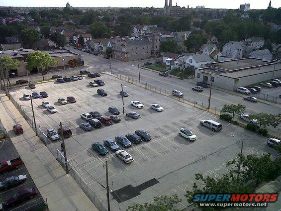 Aerial view of a large parking lot filled with various cars and some buildings in the background
