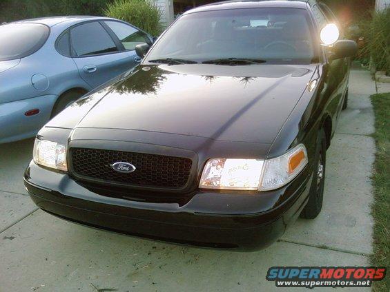 Black Ford Crown Victoria, front view, parked on driveway. Another car is visible to the left