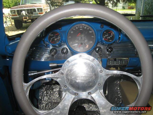 Dashboard and steering wheel of a 1956 Chevrolet, with a brown Ford pickup truck visible through the windshield