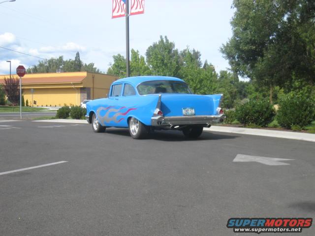 Blue 1956 Chevrolet sedan with silver and red flame decals, seen from the rear