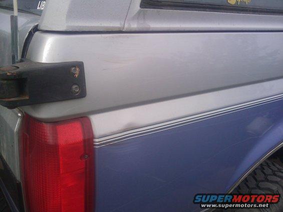 Rear quarter panel of a blue and silver Ford Bronco with a tow hitch mount. Scratches are visible on the paint