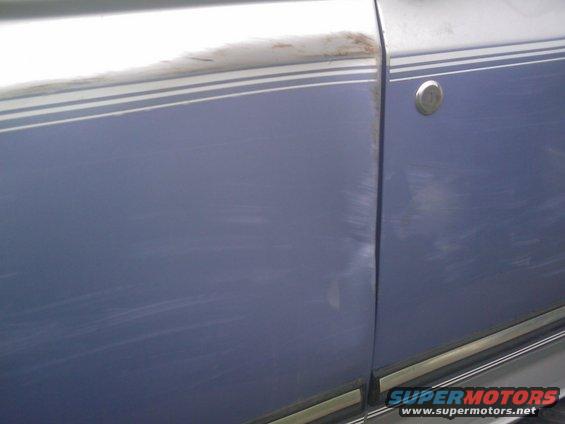 Side of a blue vehicle with a dent and scratches on the door