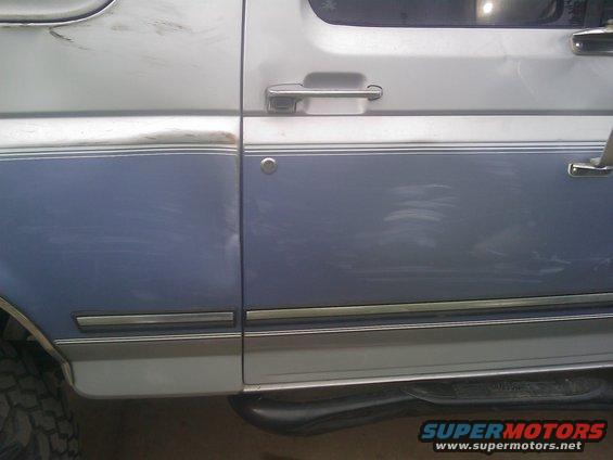 Two-tone blue and silver Ford Bronco side door with chrome trim and handle, showing scratches and dents