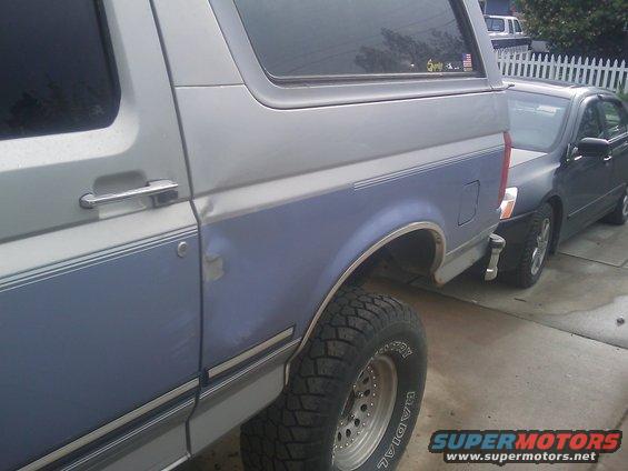 Side view of a 1996 Ford Bronco with blue and silver paint. Another car is parked behind it