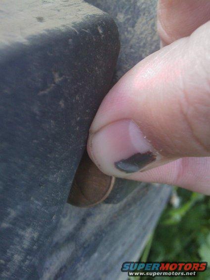 Finger pressing on a tire sidewall, showing a penny for scale
