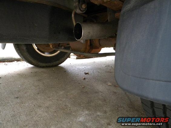 Underside view of a vehicle's exhaust pipe, rear axle, and tire