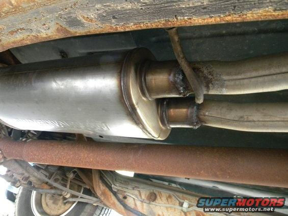 Underside of a vehicle showing a rusted exhaust pipe and muffler with visible welds