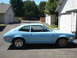 1972 Ford Pinto - A light blue 1972 Ford Pinto coupe is parked in front of a garage on a sunny day.