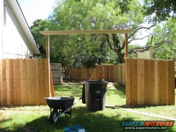 Backyard scene with wooden fence, arbor, wheelbarrow, and trash can