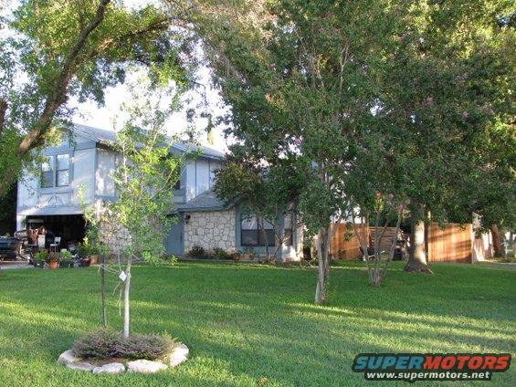 House with a well-kept lawn and trees. A vehicle is partially visible in the garage