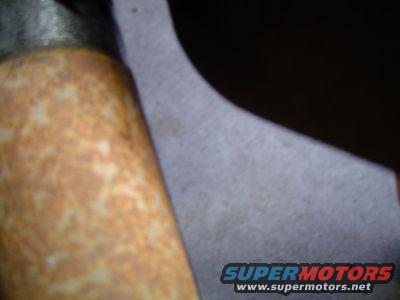 Rusted cylindrical metal part with textured surface, next to dark shadow and gray material