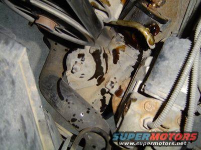 Close-up of a rusty steering gear box with fluid leaks and surrounding engine components