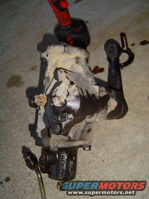 Dirty steering gear box with a red and black power tool on top, resting on concrete