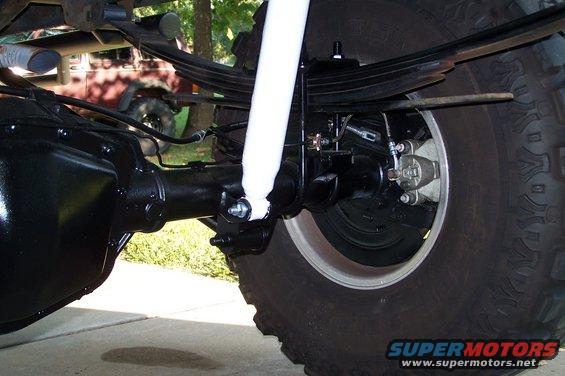 Close-up of a black rear axle, leaf springs, and a white shock absorber attached to a tire