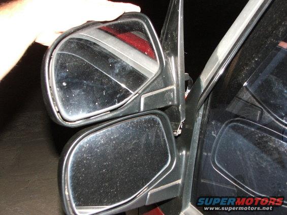Two side mirrors, one held by a hand, attached to a vehicle door frame