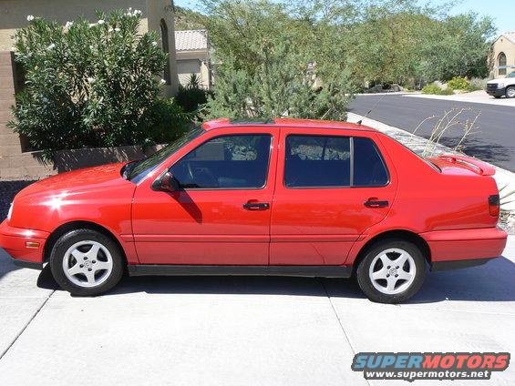 Red sedan parked on a concrete driveway with trees and a house in the background