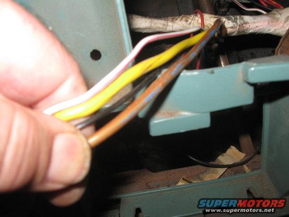 Hand holding a bundle of wires, including yellow, pink, and brown ones, near some teal-colored metal components