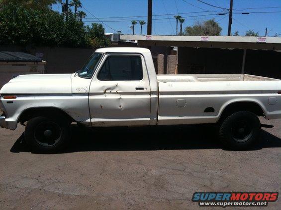 White 1979 Ford F-350 pickup truck with dents on the driver's side door and fender, black wheels, and a long bed