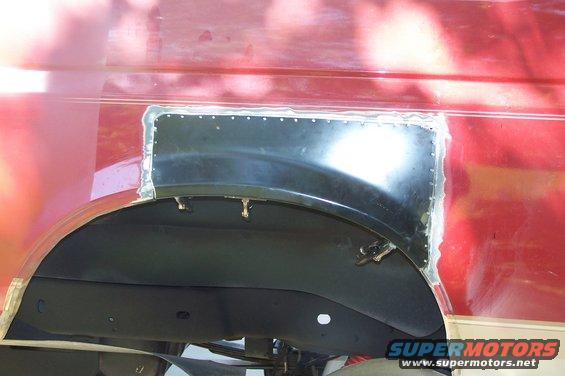 Red vehicle body panel with a black metal patch riveted over the rear wheel well opening