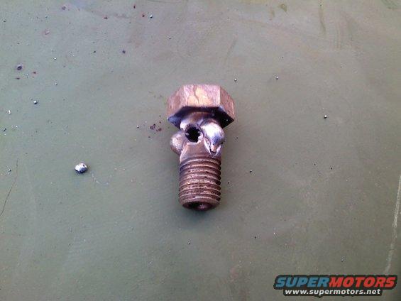 Damaged metal bolt with stripped threads and a broken head, lying on a green surface