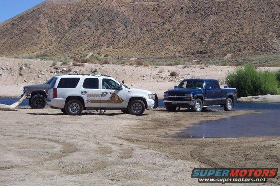 White sheriff SUV and two pickup trucks in a dry riverbed