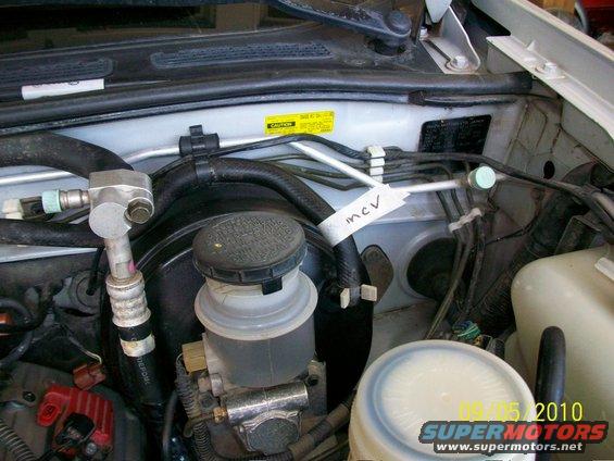 Engine bay with brake fluid reservoir and AC lines. Label says 'mcv'