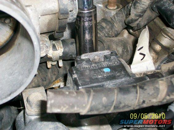 Socket wrench on black engine component with white tape marker