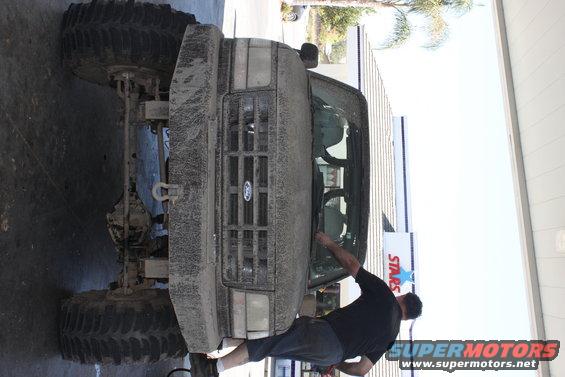 Mud-covered 1992 Ford Bronco front view with large tires and a man cleaning the windshield