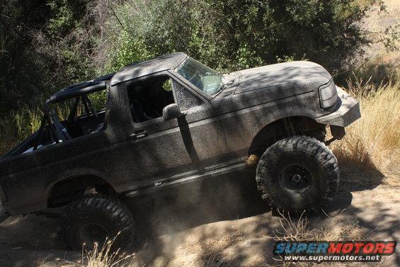 Mud-covered 1992 Ford Bronco with off-road tires climbing a dirt trail