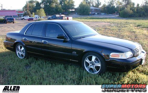 Black sedan parked on grassy area, buildings and other vehicles in background