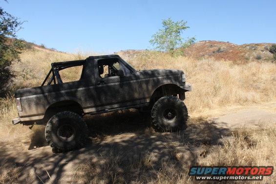 Dark-colored SUV with large tires driving on a dry, grassy hill