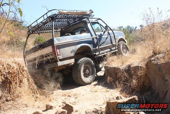 Blue 1992 Ford Bronco off-roading on a dirt trail, kicking up dust