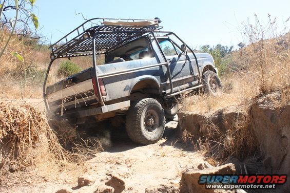1992 Ford Bronco with custom roll cage and roof rack driving off-road