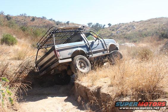 Blue off-road truck with roof rack navigating a dirt trail