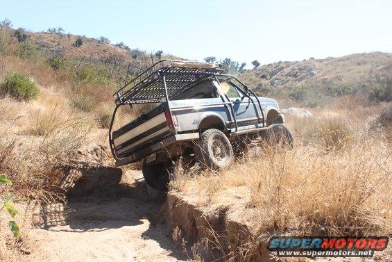 1992 Ford Bronco with roll cage and roof rack navigating a steep dirt ditch