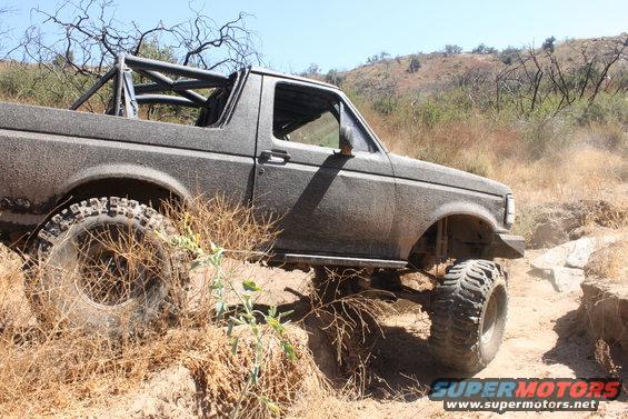 Mud-covered SUV with roll cage driving on a dirt trail
