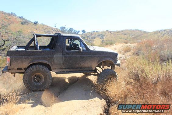 1992 Ford Bronco with roll cage driving on a dirt trail