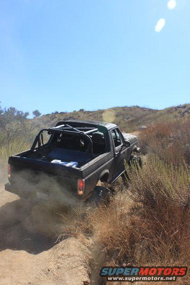 Black Ford Bronco kicking up dust on a dirt trail, roll cage visible