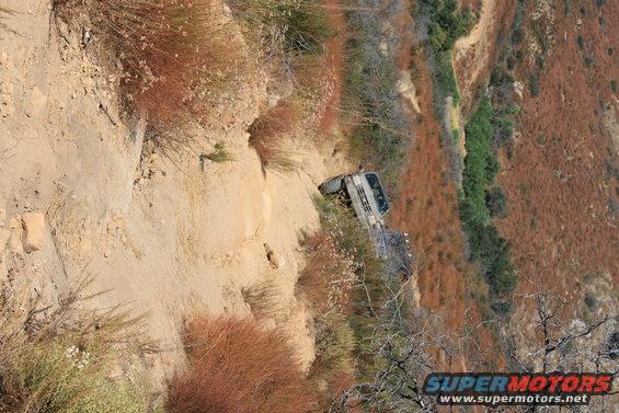 1992 Ford Bronco navigating a narrow, steep dirt trail with dry brush on either side